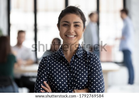 Head shot portrait close up smiling confident beautiful Indian businesswoman standing in modern office room with arms crossed, successful executive team leader mentor posing for corporate photo Royalty-Free Stock Photo #1792769584
