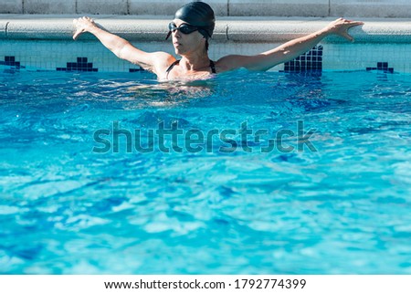 Woman with swimming cap and swimming goggles resting leaning on the curb of a swimming pool