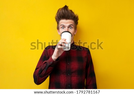 young shocked guy drinks invigorating coffee and is surprised at a yellow isolated background, a man drinks an energy drink Royalty-Free Stock Photo #1792781167