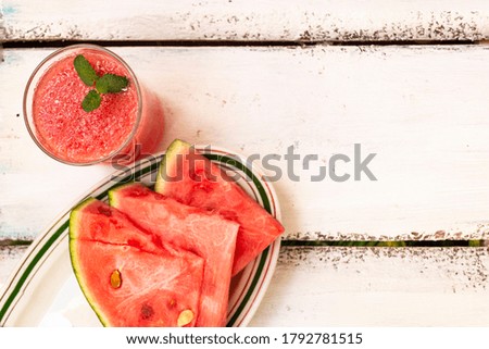 Delicious red watermelon juice with sliced fruit pieces on a plate. A sprig of mint in a glass. Copy space. Summer food concept.