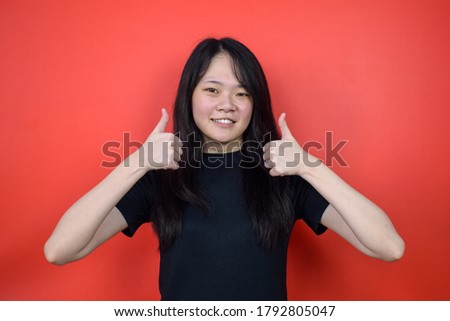 Portrait of Young beautiful asian girl using black T-shirt with red isolated background, Thumbs Up Gesture Concept