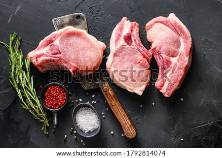Organic Pork meat chop set over american classic butcher knife or cleaver with spices and rosemary and red pepper on black slate table top view. Royalty-Free Stock Photo #1792814074