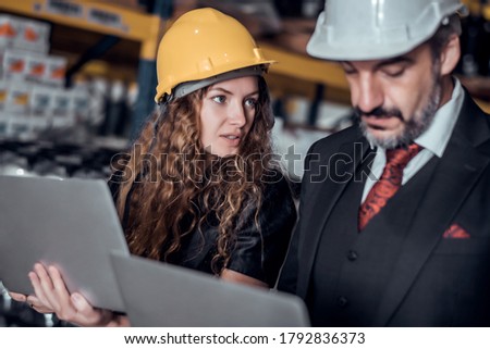 Engineer woman and businessman wearing a hardhat standing cargo at goods warehouse and check for control loading from Cargo freight ship for import and export by report on laptop. Teamwork concept