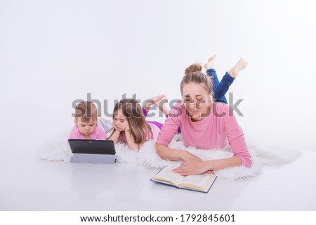a woman reads a book, children watch a cartoon on a tablet. Hobbies and recreation with gadgets. Family vacation, spend time together. home schooling
