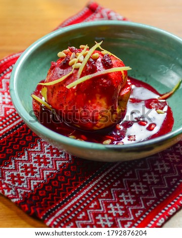 Delicious sweet baked apple with raisin, sugar sauce and walnuts served in a bowl over traditional Ukrainian red table cloth. Traditional dessert, tea time. Sugar baked apple.