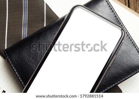 Mockup Blank white screen mobile phone. Flat lay top view of empty screen smartphone over notebook and businessman's necktie on working office desk