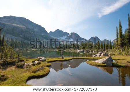 Hiker, backpacker, in the mountains, sunny day in West Kootenays, BC, Valhalla Provincial Park, Drinnon Pass. Mountains are reflecting in the water, carved lakes Royalty-Free Stock Photo #1792887373
