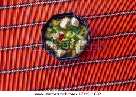 udon noodle soup with chicken and green onions on red background