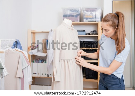 Seamstress fashion designer young woman works with mannequin, pins tailor with fabric for dress.