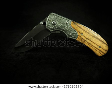 Short folding knife for carry. The handle is made of wood. With a black background.