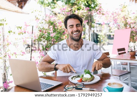 Half length portrait of cheerful caucasian male eating healthy meal satisfied with brunch laughing in good mood, positive funny hipster guy keeping healthy lifestyle enjoying vegan food in cafe Royalty-Free Stock Photo #1792949257