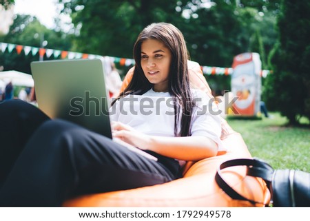 Smiling beautiful female enjoying working on freelance in park making research browsing web pages, cheerful millennial woman 20s freelancer typing on laptop computer chatting in social networks