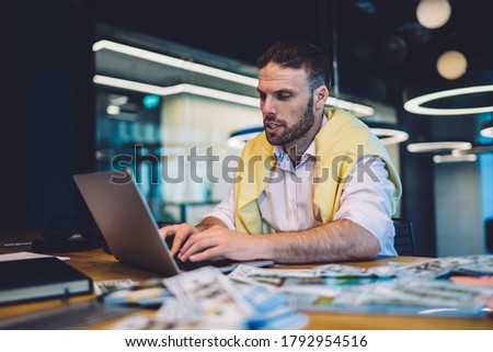 Professional trader using 4g wireless internet connection on modern laptop technology while making online money sitting at coworking table with dollars wad, smart casual businessman watching webinar
