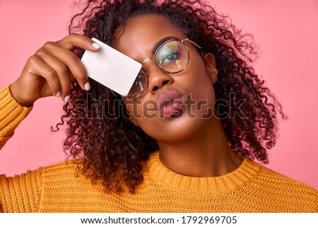 Portrait of a dark skinned curly woman in glasses and a yellow sweater with a mockup credit card in her hands in a photo studio on a pink background. The concept of easy banking, advertising.
