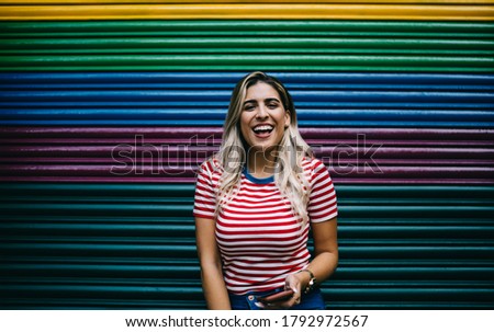 Half length portrait of cheerful Spanish hipster girl laughing at camera during smartphone blogging at colorful copy space, grinning female millennial satisfied with leisure pastime at publicity area Royalty-Free Stock Photo #1792972567