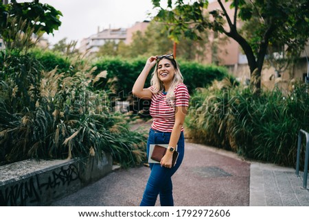 Half length portrait of trendy casually dressed blonde hipster girl posing in park on weekend trip, positive young caucasian woman student looking at camera enjoying spending leisure outdoor