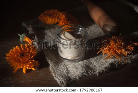 Herbal cosmetics with calendula flowers on blue background. Homemade natural cream.