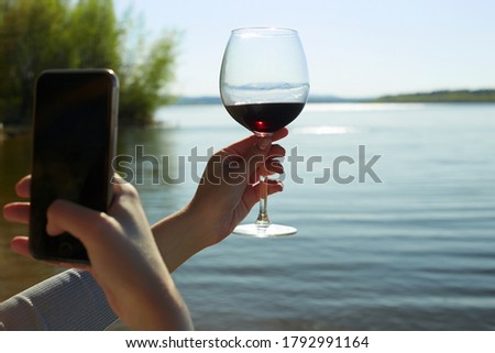 girl photographs a glass of wine in her handon smartphone. Female hand with Wine on Nature