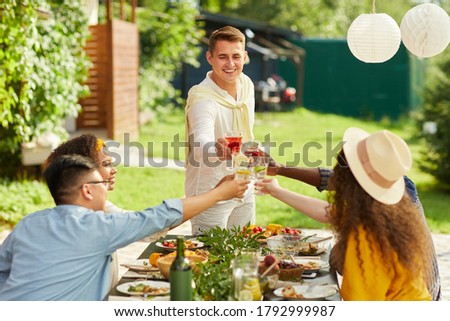 Portrait of smiling young man toasting with friends while enjoying dinner at outdoor terrace in Summer, copy space