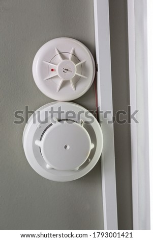 Two white smoke detector and fire sprinkler on a light ceiling. Vertical orientation. Fire alarm.