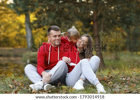 little daughter kissing and hugging her mom and dad in the autumn park. The concept of family holiday. Father's, mother's, baby's day. Spending time together. Family look.