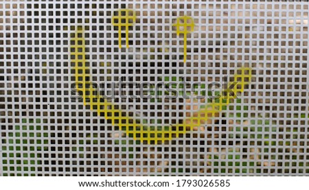 Metal grid. Metal fence. Graffiti on the fence. Drawing with paint on the wall. Smiley.