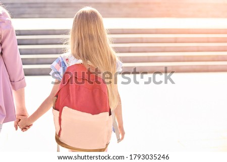 Little girl hold mother hand. Back to school. Schoolbag uniform at city. Young student. Summer education. Childhood concept. Learning in preschool. Sun light road. Copyspace