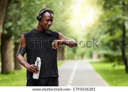 Modern technologies and active lifestyle. African sportsman working out with fitness bracelet, drinking water, blurred park background, copy space Royalty-Free Stock Photo #1793036281