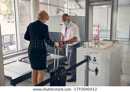 Male airport worker in medical face mask taking travel suitcase from blonde woman Royalty-Free Stock Photo #1793040412
