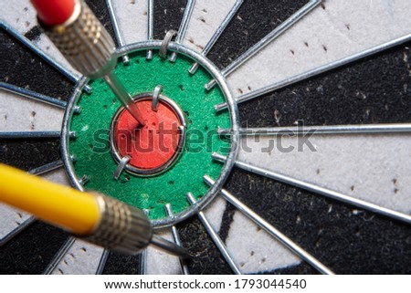 Blurred background in soft focus with a darts board with a closeup of an arrow hitting the center and an opponent's arrow stuck nearby. Concept - fierce competition in business