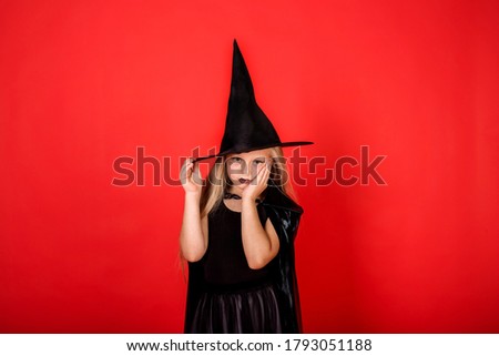 upset girl in a witch costume with a hat on a red background with a copy of space