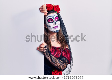Young woman wearing day of the dead custome holding blank empty banner smiling looking to the side and staring away thinking. 