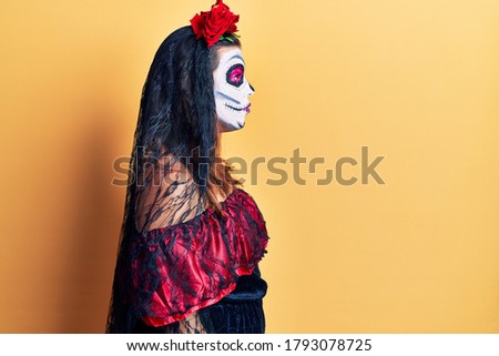 Young woman wearing day of the dead costume over yellow looking to side, relax profile pose with natural face with confident smile. 