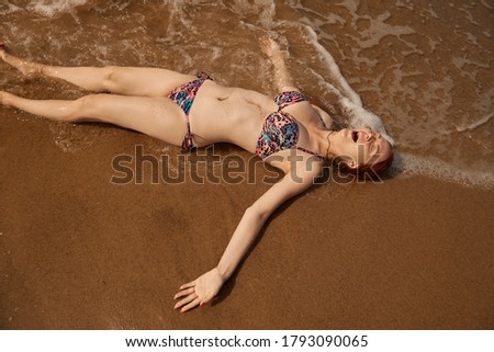 single happy young red hair woman in bikini lying at sea surf with splashes