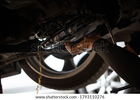 Car mechanic drains the old automatic transmission fluid (ATF) or gear oil at car garage for changing the oil in a gear box of car engine Royalty-Free Stock Photo #1793110276