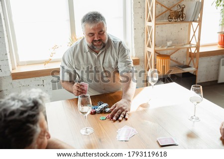 Young at heart. Two happy mature friends playing cards and drinking wine. Look delighted, excited. Caucasian men gambling at home. Sincere emotions, wellbeing, facial expression concept. Smiling.