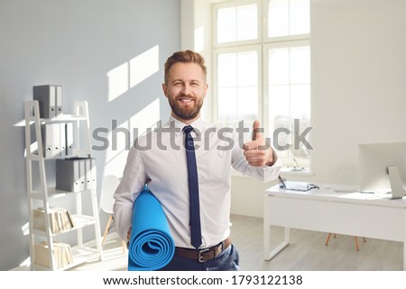 Happy successful businessman in a white shirt with yoga mat standing in the office.