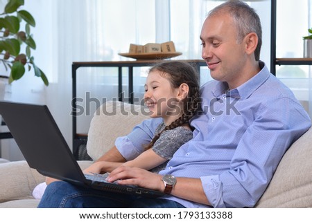 Happy family, happy dad and daughter laugh and watch cartoons, funny programs in a laptop during quarantine. Leisure, fun, online entertainment