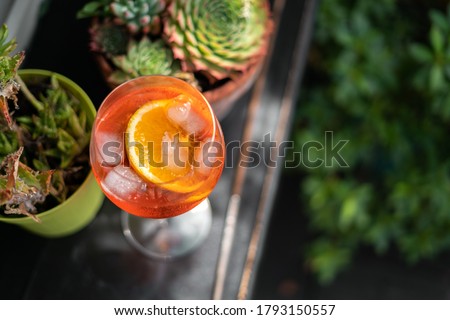 Red Aperol Spritz cocktail drink with ice and slice of orange on the green rooftop garden bar. Typical refreshing drink in Italy. Holiday - party - relax concept photo with green natural background. Royalty-Free Stock Photo #1793150557
