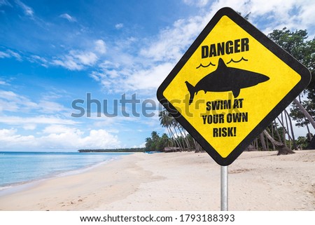 A shark warning sign at the beach. Shark season or shark infested waters. A stern warning to bathers that they are at great risk. Tropical beach setting.