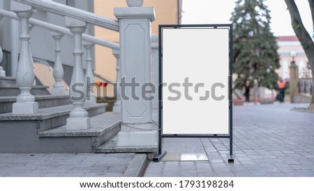 white mock-up in black metal frame stands on pavement of city street staircase with marble railing background outside