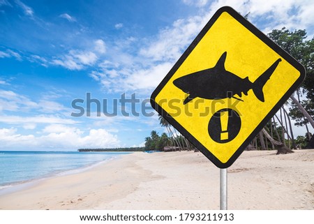 A shark warning sign at the beach. Shark season or shark infested waters. A stern warning to bathers that they are at great risk. Tropical beach setting.