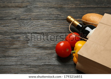Paper bag with different food on wooden background, space for text