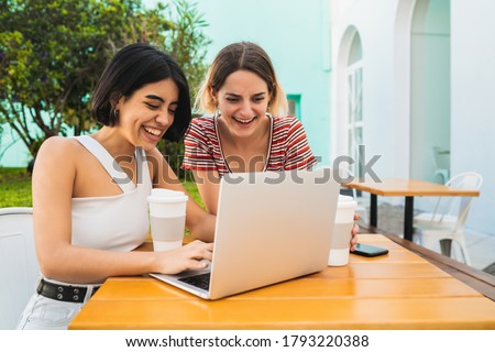 Portrait of two young friends using a laptop at coffee shop. Technology and friendship concept.