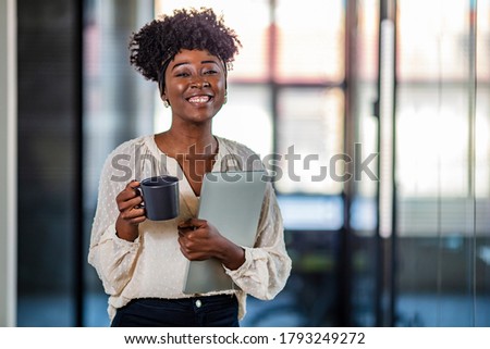 Woman standing with arms crossed in a modern bright office. Businesswoman With laptop By Window Of New Office. Mid adult black businesswoman analyzing reports in the office and looking at camera Royalty-Free Stock Photo #1793249272