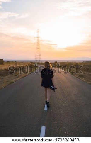 white girl catching skateboard on her back in the middle of the road at sunset