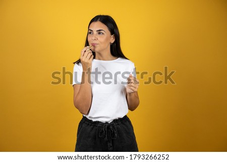Young beautiful woman painting her lips with a red lipstick. Looking to the left on yellow background. Beauty concept