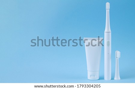 Smart electric toothbrush with spare head and toothpaste on blue background. Professional oral care concept