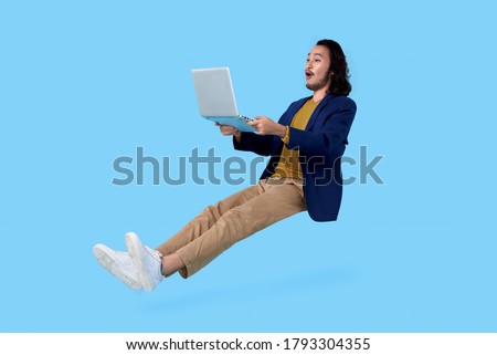 Young asian businessman hand holding computer laptop floating in mid-air isolated on blue background.
