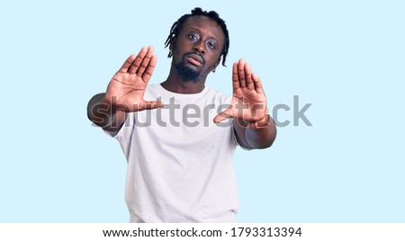 Young african american man with braids wearing casual white tshirt doing frame using hands palms and fingers, camera perspective 